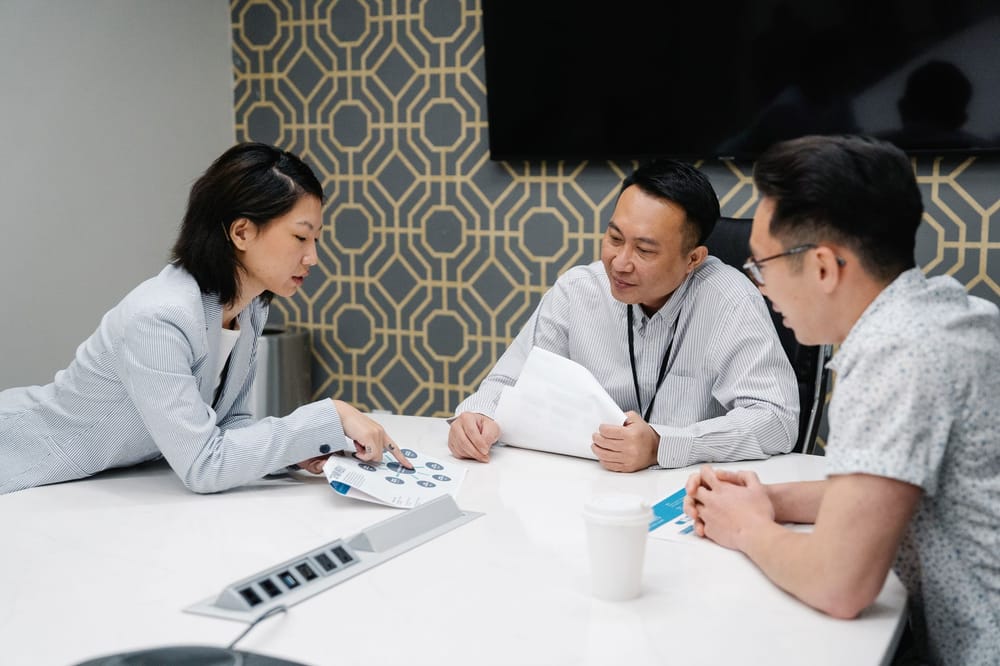 Three colleagues reviewing printed documents together around an office desk